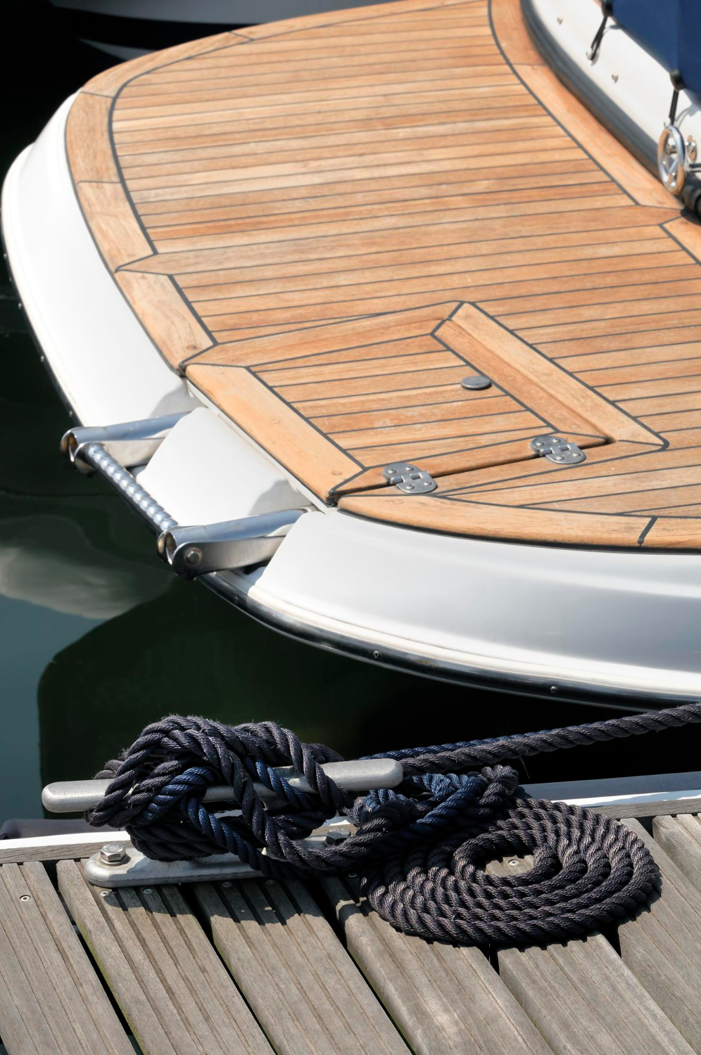 Coperta in teak di una barca a motore ormeggiata, con cima sulla bitta del pontile